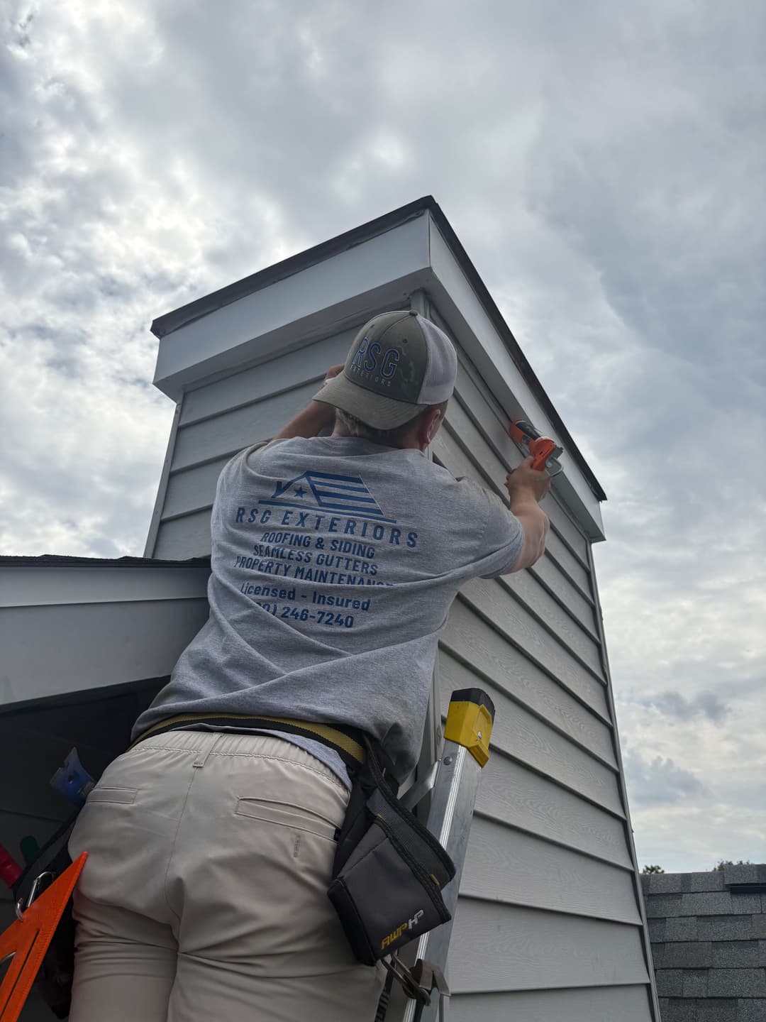 Contractor performing roof maintenance on a residential building under cloudy skies.