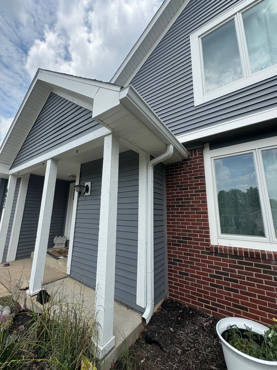 Modern home exterior with gray siding and brick accents, featuring a spacious porch and windows.