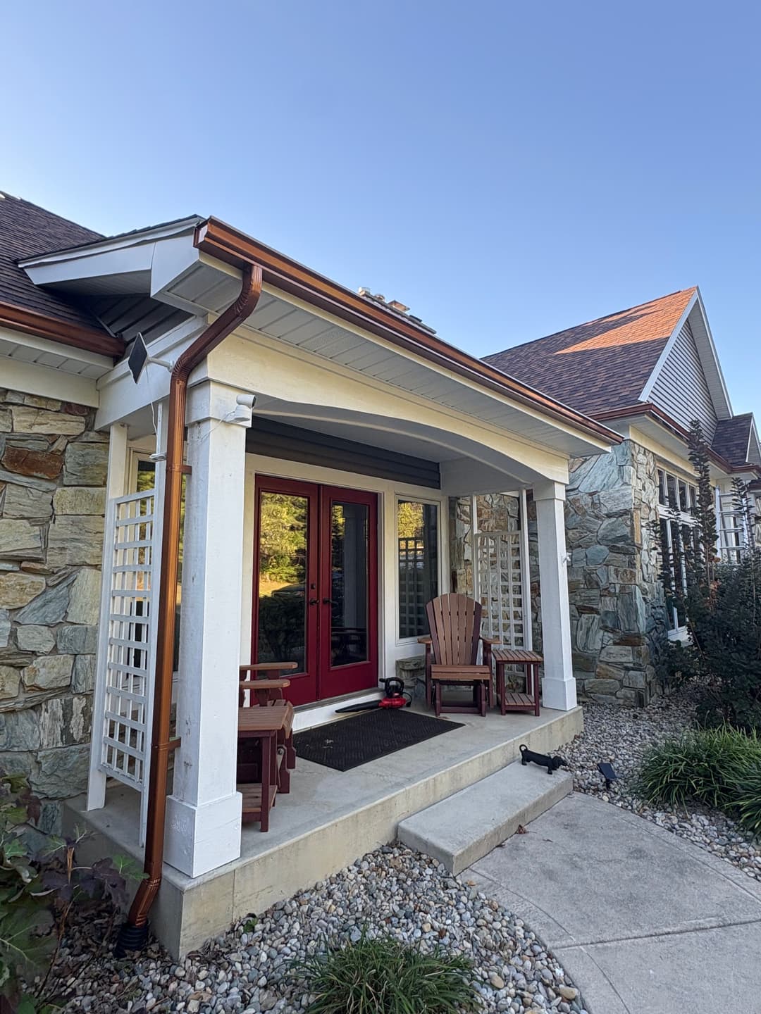 Charming stone house with red front door, porch seating, and lush landscaping.