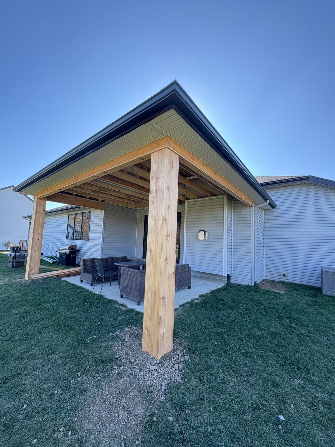 Modern home exterior featuring a wooden patio structure and outdoor seating area.