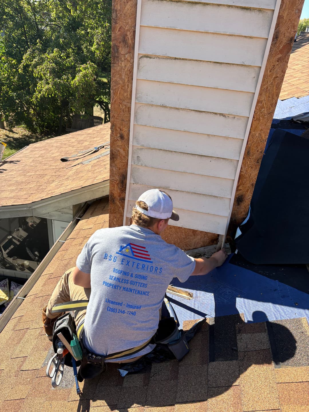 Worker repairing siding on a residential roof, showcasing construction and maintenance expertise.